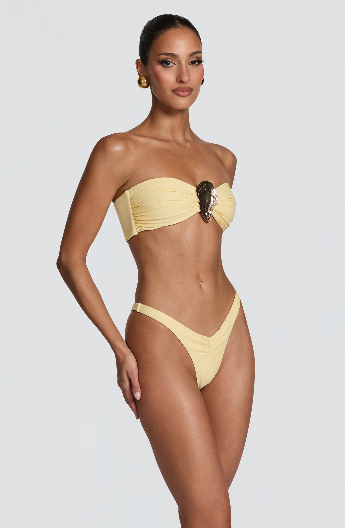 Top de bikini bandeau amarillo limón con adorno dorado ovalado y frunces en copa