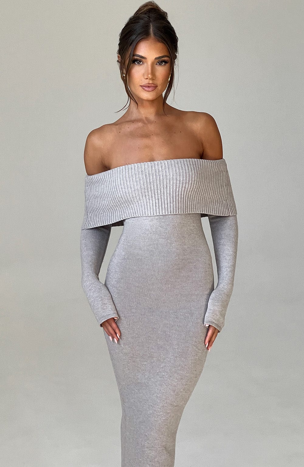 Vestido largo de punto gris claro con hombros descubiertos, manga caída y falda ajustada.