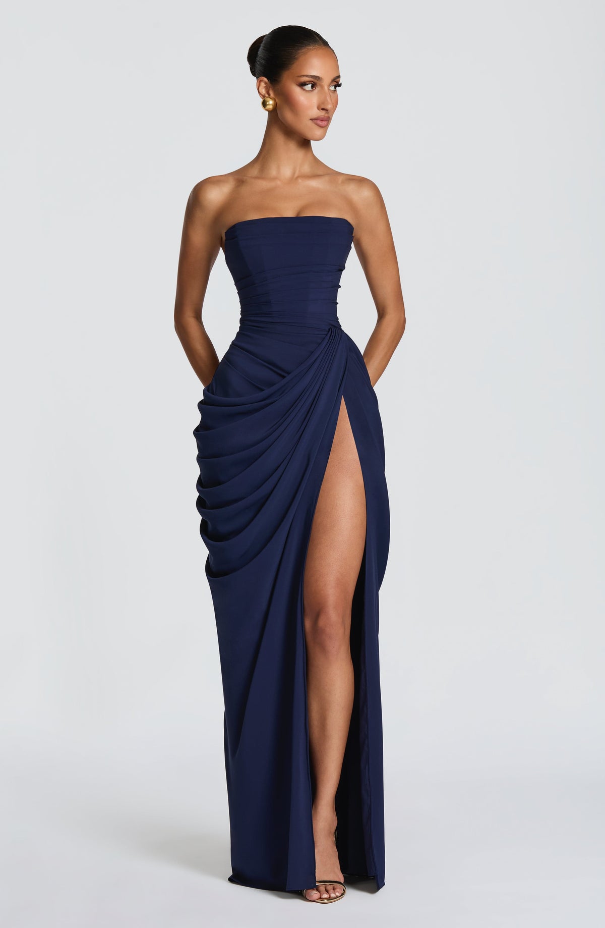 Vestido largo azul oscuro strapless con drapeado envolvente y abertura lateral en la pierna.