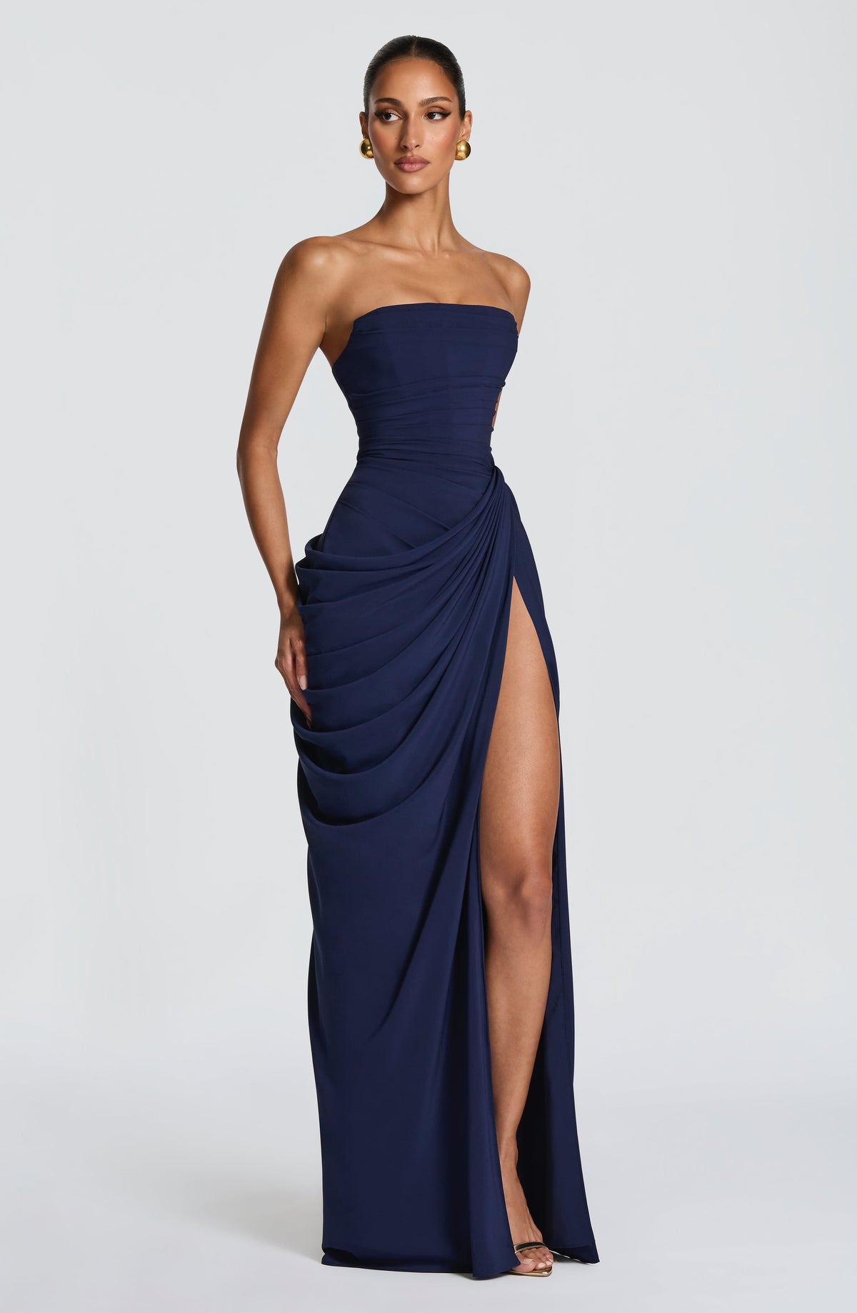 Vestido largo azul oscuro strapless con drapeado en capas y abertura frontal pronunciada.