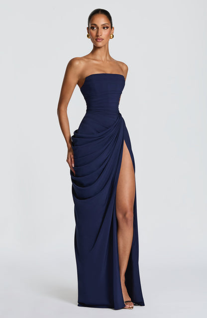 Vestido largo azul oscuro strapless con drapeado en capas y abertura frontal pronunciada.