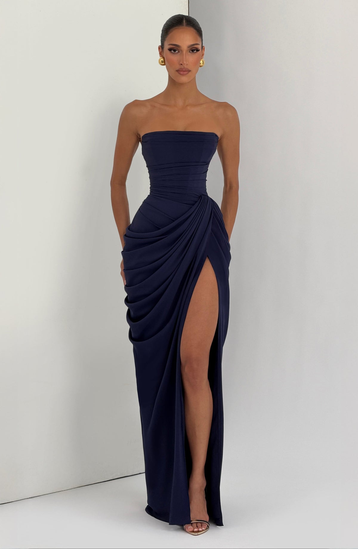 Vestido largo azul oscuro strapless con drapeado envolvente y abertura hasta la rodilla.