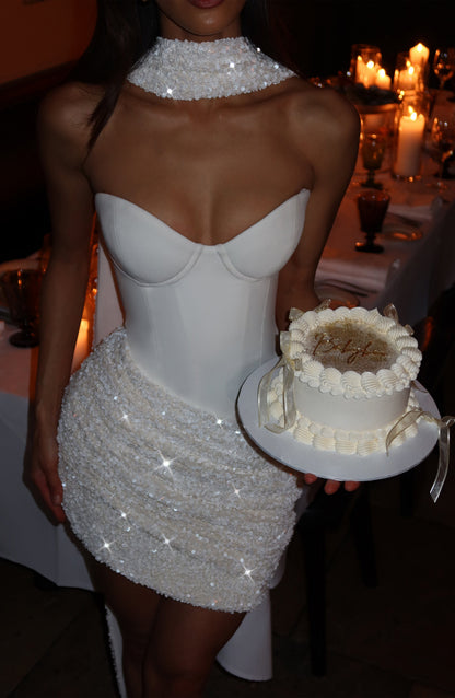 Vestido blanco sin mangas con escote corazón y acabado brillante con falda corta.
