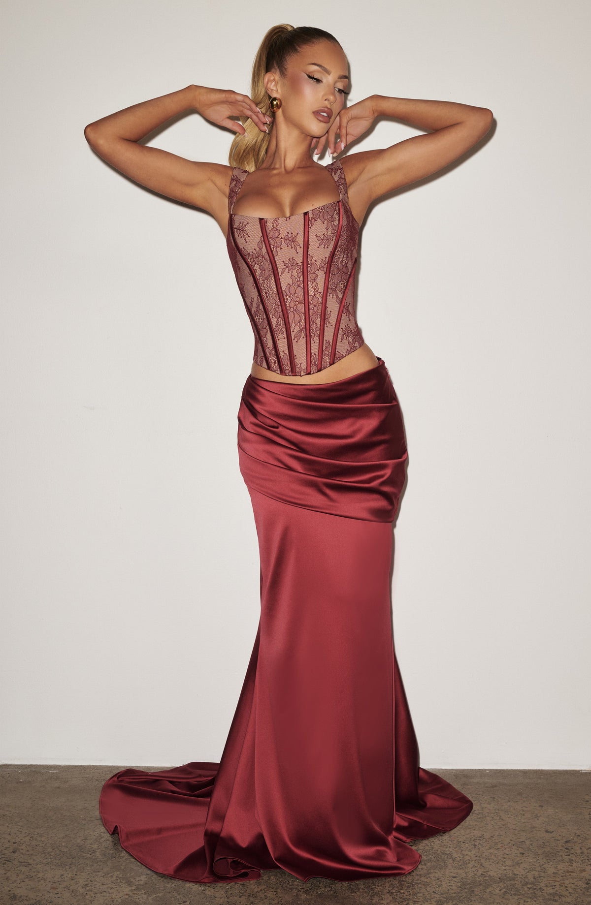 Vestido corsé de encaje burdeos con falda larga satinada y drapeado envolvente.