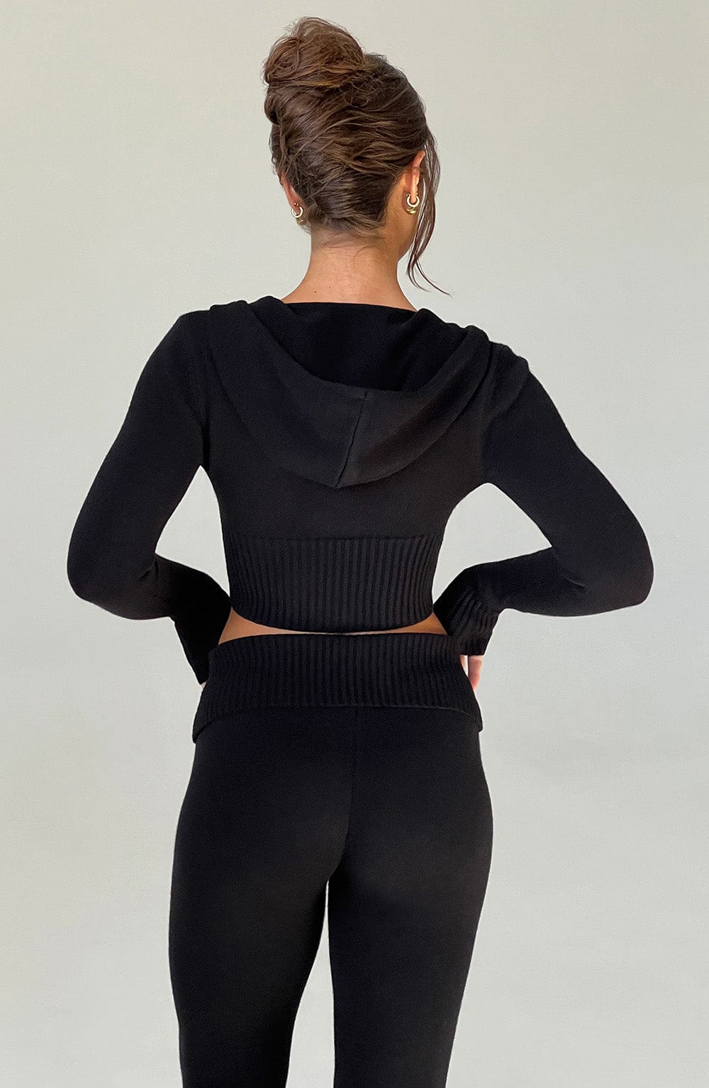 Sudadera negra con capucha, vista trasera con tejido acanalado y cintura entallada.