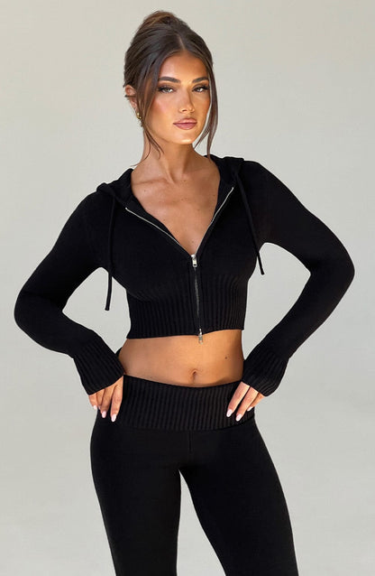 Sudadera negra con capucha y cremallera, tejido acanalado en mangas y cintura corta.