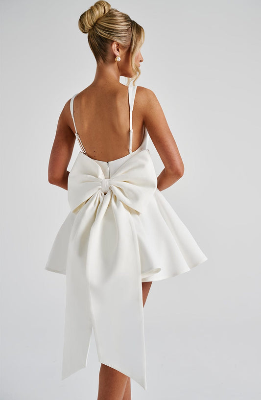 Vestido blanco de espalda descubierta con lazo central y falda con vuelo plisado.