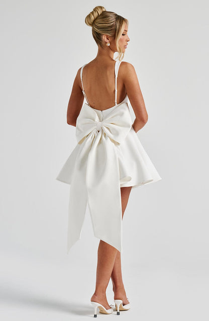 Vestido blanco de espalda descubierta con lazo central y falda con vuelo y cintas largas.