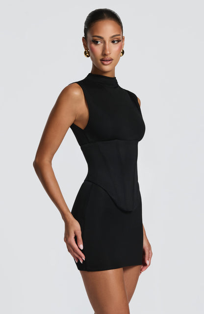 Vestido negro sin mangas con cuello alto y frunce en la cintura, vista lateral